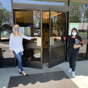 Two women wearing masks and opening doors to Redwood Credit Union.